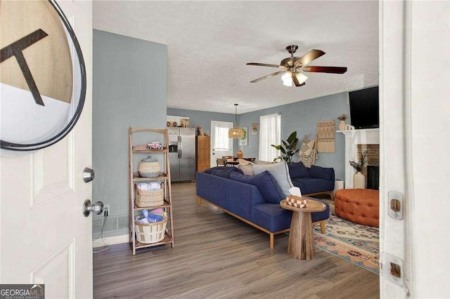 living room with a textured ceiling, ceiling fan, and wood-type flooring