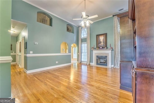 unfurnished living room with a towering ceiling, light hardwood / wood-style floors, ornamental molding, and ceiling fan