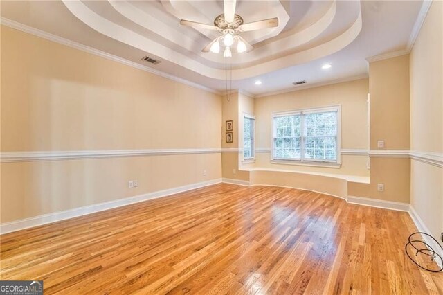 spare room featuring light hardwood / wood-style floors, a raised ceiling, ornamental molding, and ceiling fan