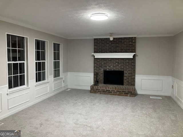 unfurnished living room with a brick fireplace, a textured ceiling, crown molding, and carpet