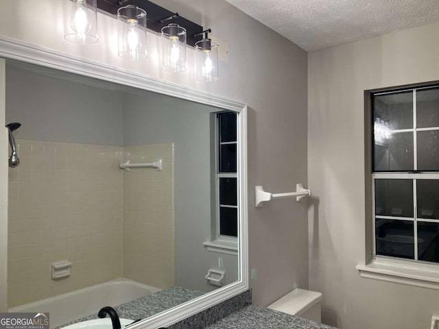 bathroom featuring a textured ceiling, tiled shower / bath combo, and toilet