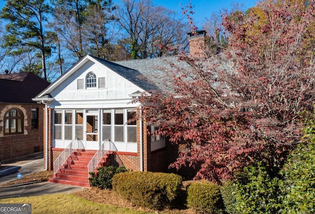 exterior space with stairs, brick siding, a sunroom, and a chimney