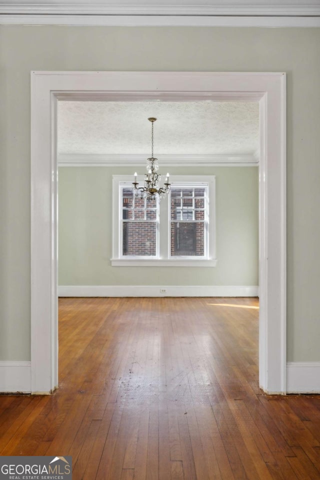 unfurnished dining area with an inviting chandelier, hardwood / wood-style flooring, baseboards, and ornamental molding