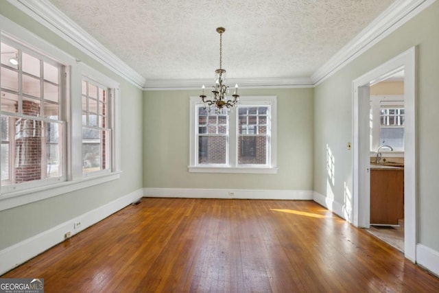 unfurnished dining area with baseboards, a chandelier, ornamental molding, and hardwood / wood-style flooring