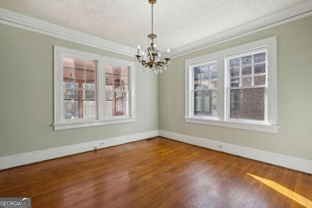 unfurnished dining area with baseboards, an inviting chandelier, ornamental molding, hardwood / wood-style flooring, and a textured ceiling