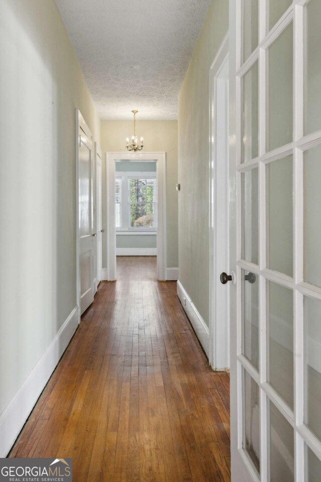 corridor with hardwood / wood-style flooring, a notable chandelier, baseboards, and a textured ceiling