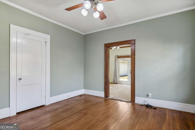 spare room featuring ceiling fan, baseboards, wood finished floors, and crown molding