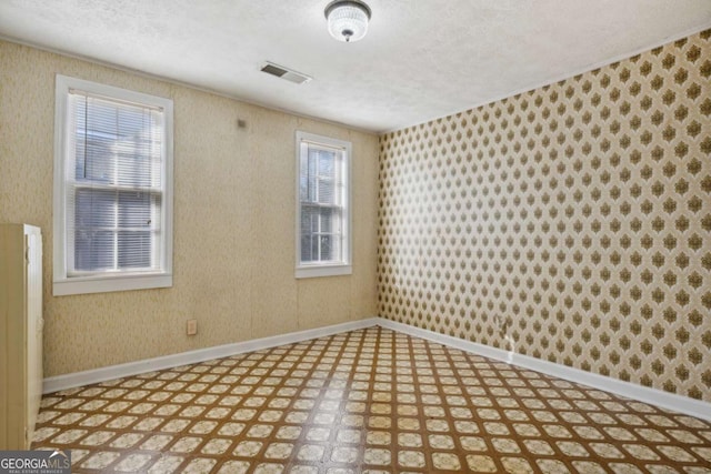 unfurnished room with visible vents, baseboards, light floors, and wallpapered walls