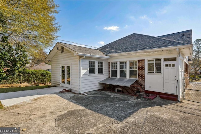 rear view of property featuring a patio, fence, roof with shingles, entry steps, and brick siding