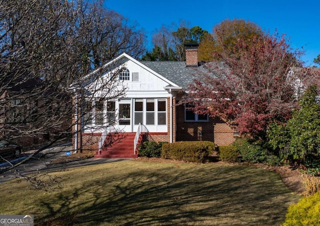 view of front of home featuring brick siding, a chimney, a front lawn, and roof with shingles