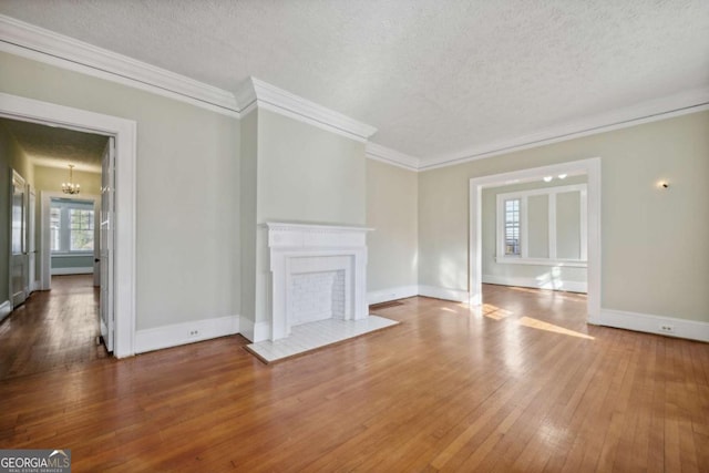 unfurnished living room with an inviting chandelier, a fireplace with flush hearth, ornamental molding, wood-type flooring, and a textured ceiling