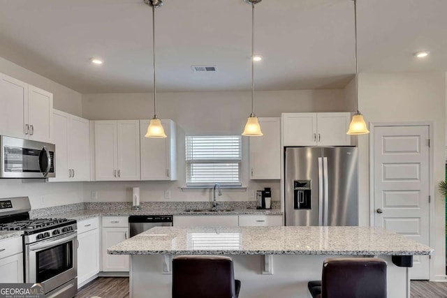 kitchen with stainless steel appliances, a kitchen island, white cabinetry, a kitchen breakfast bar, and sink