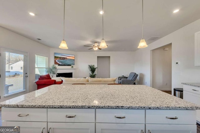 kitchen featuring white cabinets, light stone countertops, ceiling fan, and hanging light fixtures