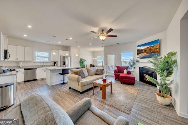 living room featuring sink, ceiling fan, and light wood-type flooring