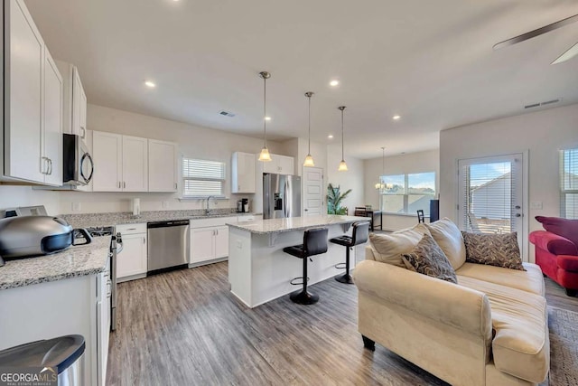 kitchen featuring a kitchen breakfast bar, stainless steel appliances, a center island, white cabinetry, and decorative light fixtures