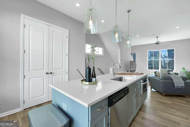 kitchen with a center island with sink, stainless steel appliances, decorative light fixtures, light hardwood / wood-style floors, and sink