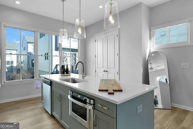 kitchen with light hardwood / wood-style flooring, an island with sink, stainless steel appliances, pendant lighting, and sink