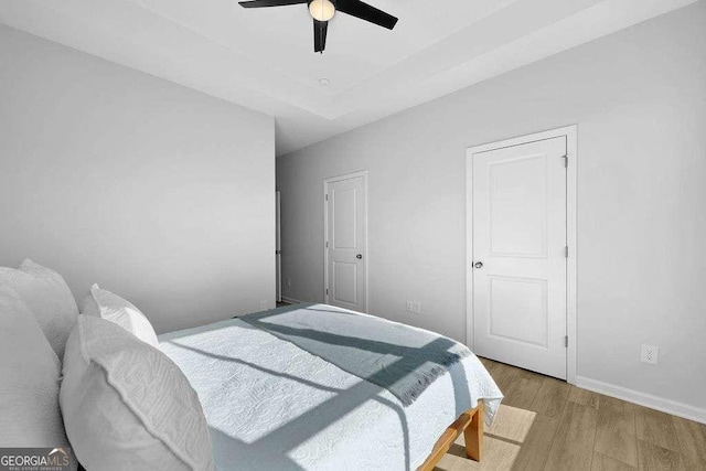 bedroom featuring a tray ceiling, ceiling fan, and light hardwood / wood-style floors