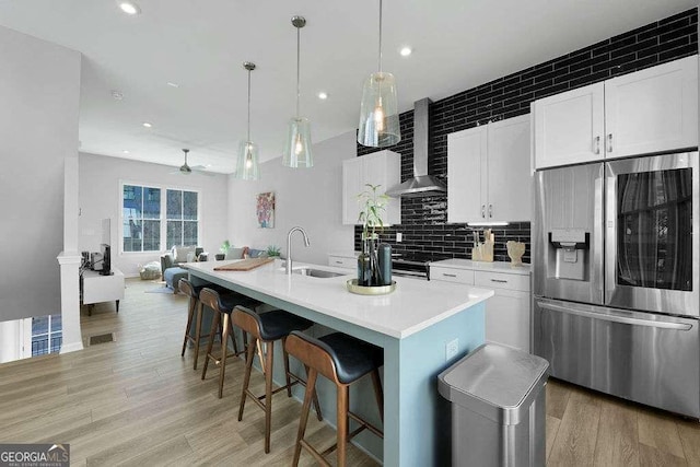 kitchen with wall chimney exhaust hood, an island with sink, white cabinets, sink, and stainless steel fridge with ice dispenser