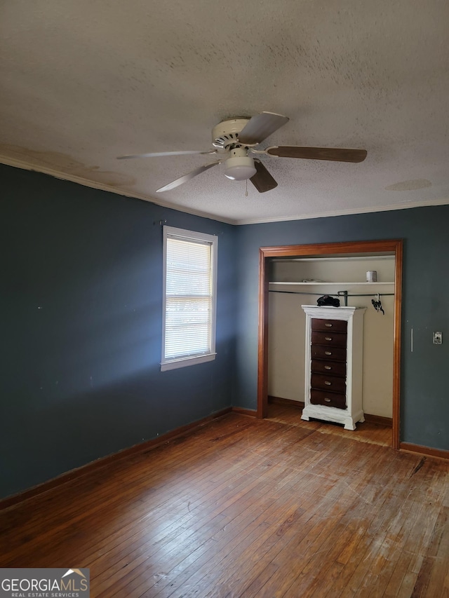 unfurnished bedroom with a textured ceiling, ceiling fan, a closet, and hardwood / wood-style floors