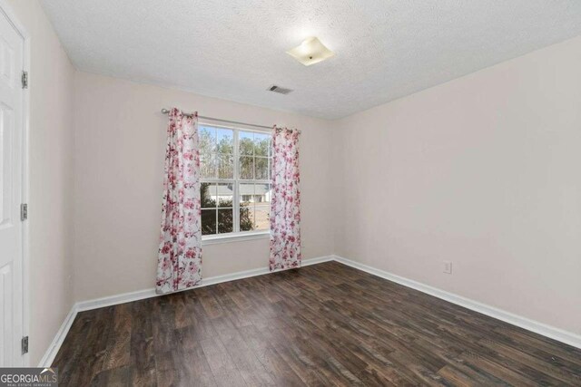 empty room with a textured ceiling and dark hardwood / wood-style floors