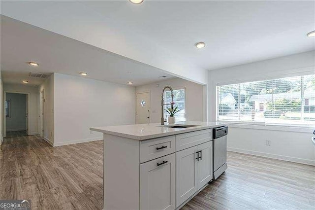 kitchen with white cabinets, a center island with sink, light hardwood / wood-style floors, sink, and stainless steel dishwasher