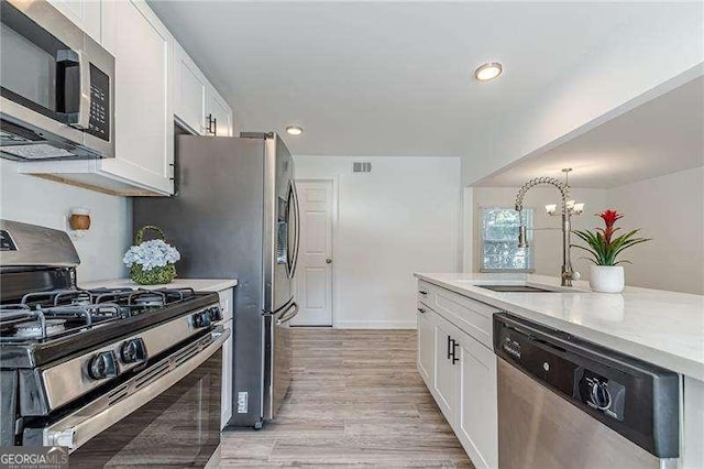 kitchen featuring pendant lighting, a notable chandelier, white cabinets, appliances with stainless steel finishes, and sink