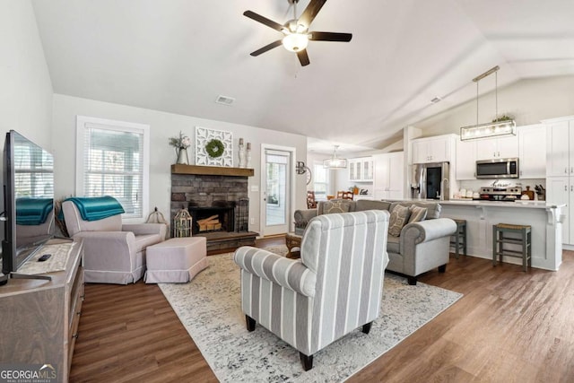 living room with light hardwood / wood-style flooring, a stone fireplace, vaulted ceiling, and a wealth of natural light