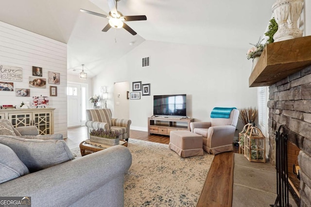 living room featuring hardwood / wood-style flooring, ceiling fan, vaulted ceiling, and a stone fireplace