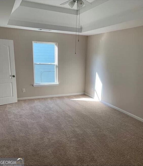 carpeted empty room with ceiling fan and a tray ceiling