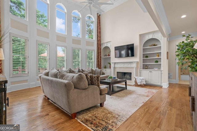 living room with light hardwood / wood-style flooring, built in features, ceiling fan, a towering ceiling, and ornamental molding