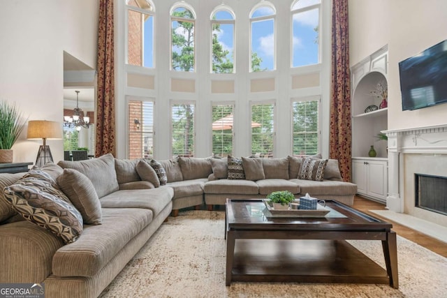 living room featuring hardwood / wood-style flooring, built in features, a high ceiling, a high end fireplace, and a chandelier