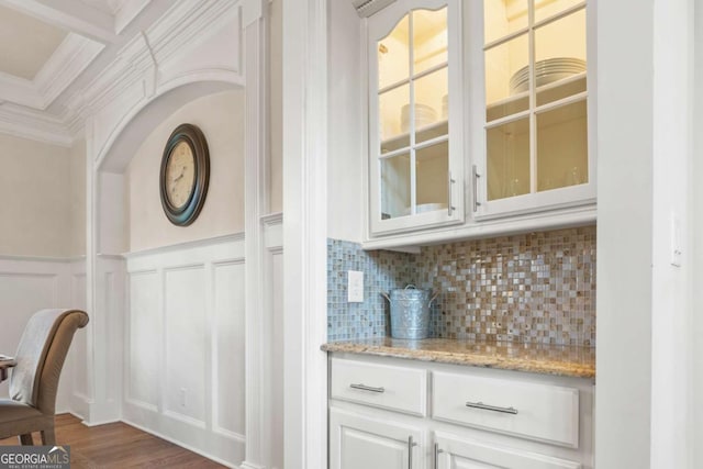 bar with dark hardwood / wood-style floors, tasteful backsplash, white cabinetry, light stone counters, and crown molding