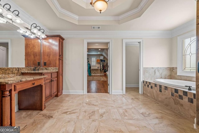 bathroom featuring vanity, tiled tub, a tray ceiling, and ornamental molding