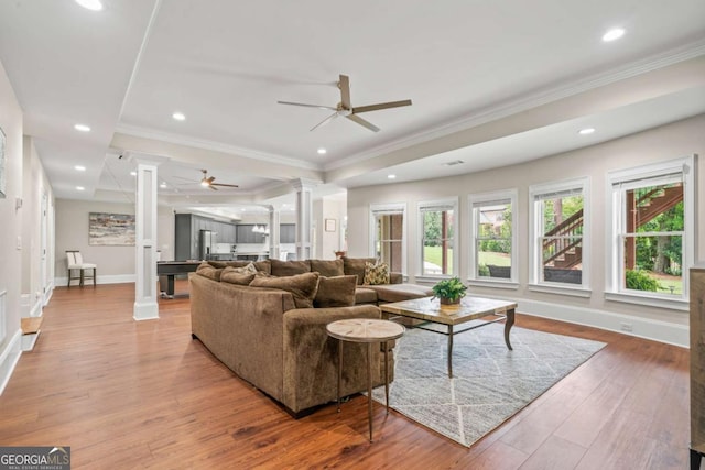 living room featuring ornate columns, wood-type flooring, ornamental molding, ceiling fan, and a tray ceiling