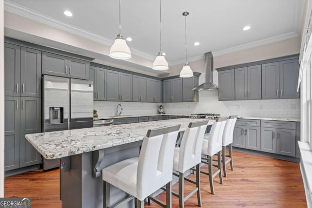 kitchen with a breakfast bar area, a kitchen island, hanging light fixtures, and wall chimney range hood