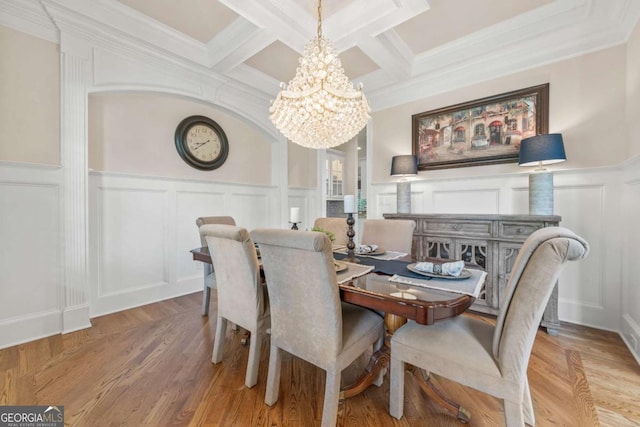 dining space with crown molding, beam ceiling, coffered ceiling, light hardwood / wood-style floors, and a chandelier