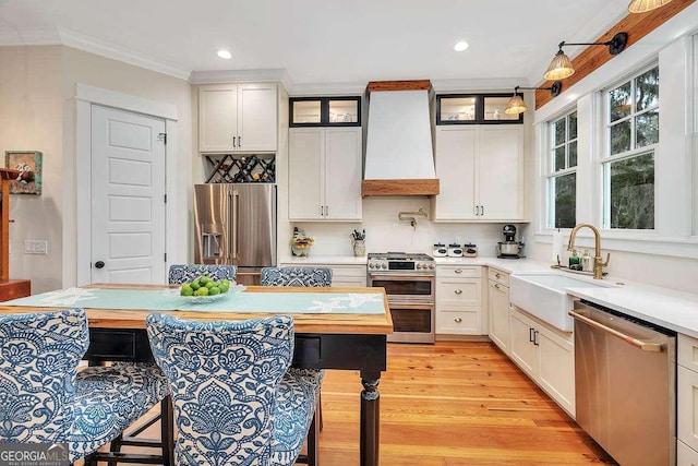 kitchen with sink, premium range hood, stainless steel appliances, white cabinets, and decorative light fixtures