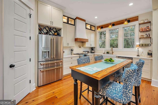 kitchen featuring light wood-style flooring, high end fridge, light countertops, premium range hood, and a sink