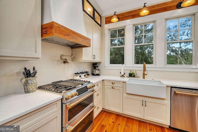 kitchen with pendant lighting, sink, premium range hood, appliances with stainless steel finishes, and light hardwood / wood-style floors