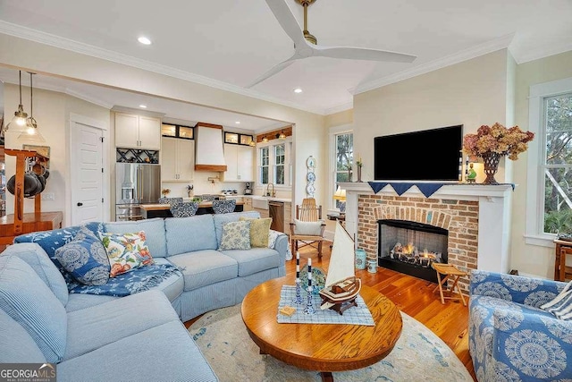 living room with crown molding, a brick fireplace, and light wood-style floors