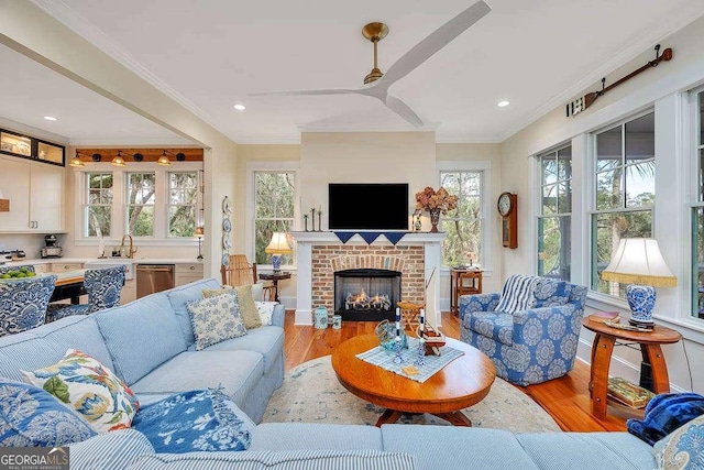 living room featuring a fireplace, ornamental molding, ceiling fan, and light wood-type flooring