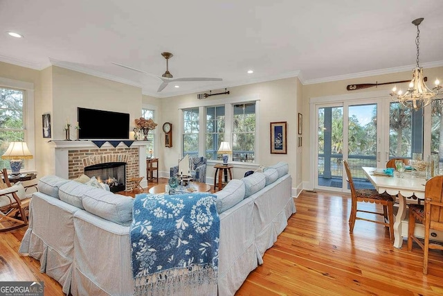 living room featuring a brick fireplace, ceiling fan with notable chandelier, plenty of natural light, and light hardwood / wood-style floors