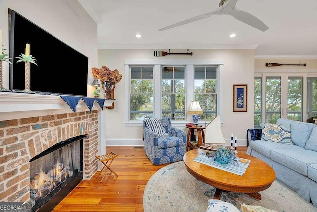 living room featuring ceiling fan, ornamental molding, a fireplace, and light hardwood / wood-style floors