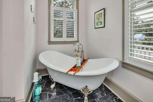 bathroom with marble finish floor, plenty of natural light, and a freestanding bath