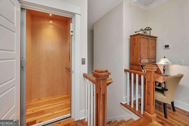 interior space with visible vents, elevator, an upstairs landing, wood finished floors, and baseboards