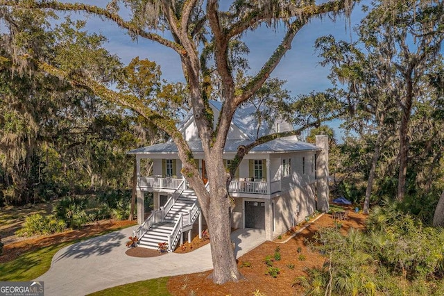 coastal home featuring metal roof, a porch, stairs, driveway, and a chimney