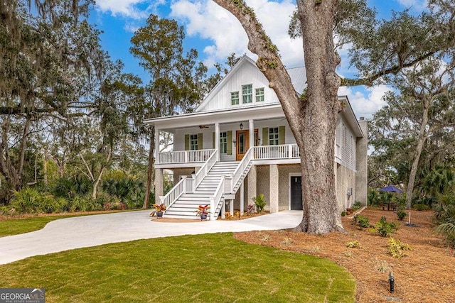 coastal inspired home featuring driveway, covered porch, stairs, a front lawn, and board and batten siding