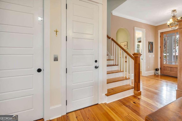 foyer entrance with crown molding, light hardwood / wood-style floors, and a notable chandelier