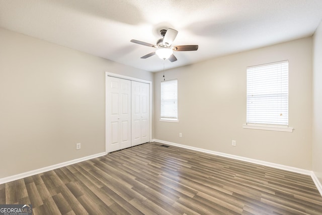 unfurnished bedroom with ceiling fan, dark wood-type flooring, and a closet